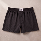 Black and dark gray vertically striped boxer briefs with a white waistband label reading 'GB', laid flat on a light beige textured background.