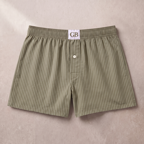 A pair of men's boxer shorts in an olive green and white vertical stripe pattern, laid flat on a neutral beige background. A white fabric tag with 'GB' is visible at the waistband.